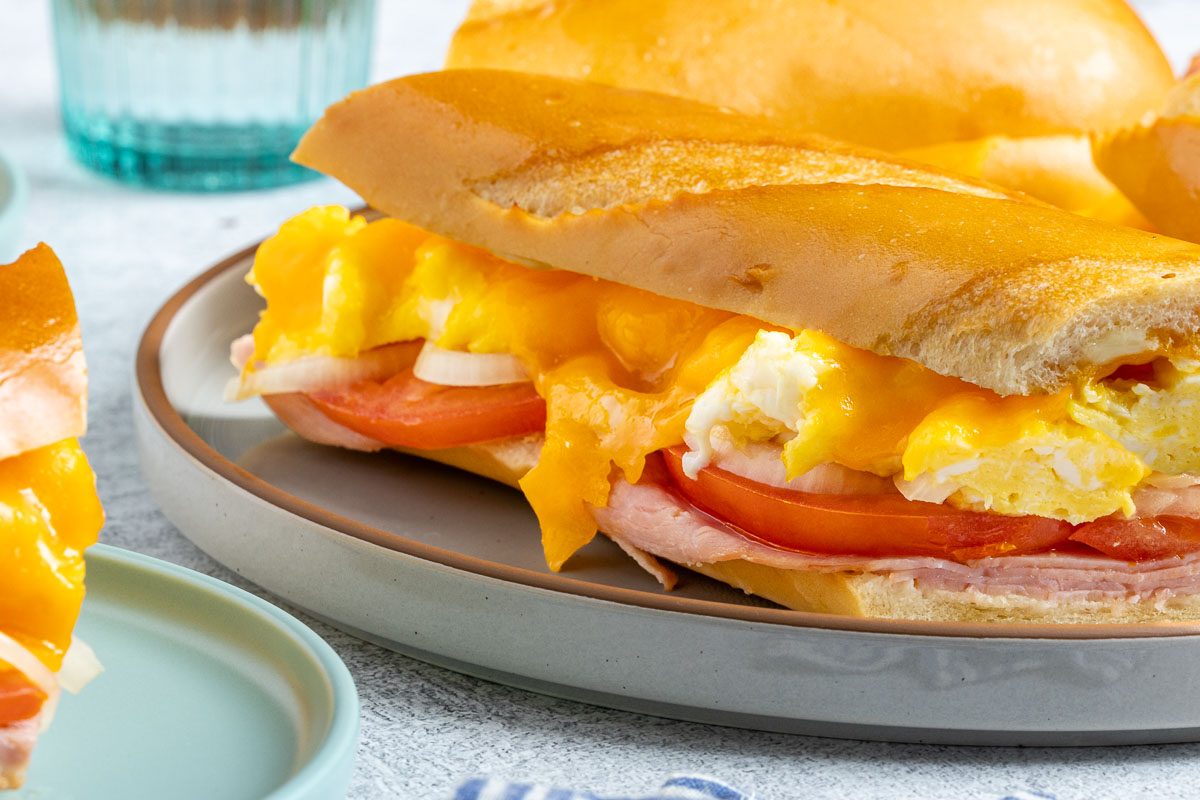 Taste of Home Ham Egg and Cheese Sandwich recipe photo of the sandwich cut into slices and set on a serving platter and plates.