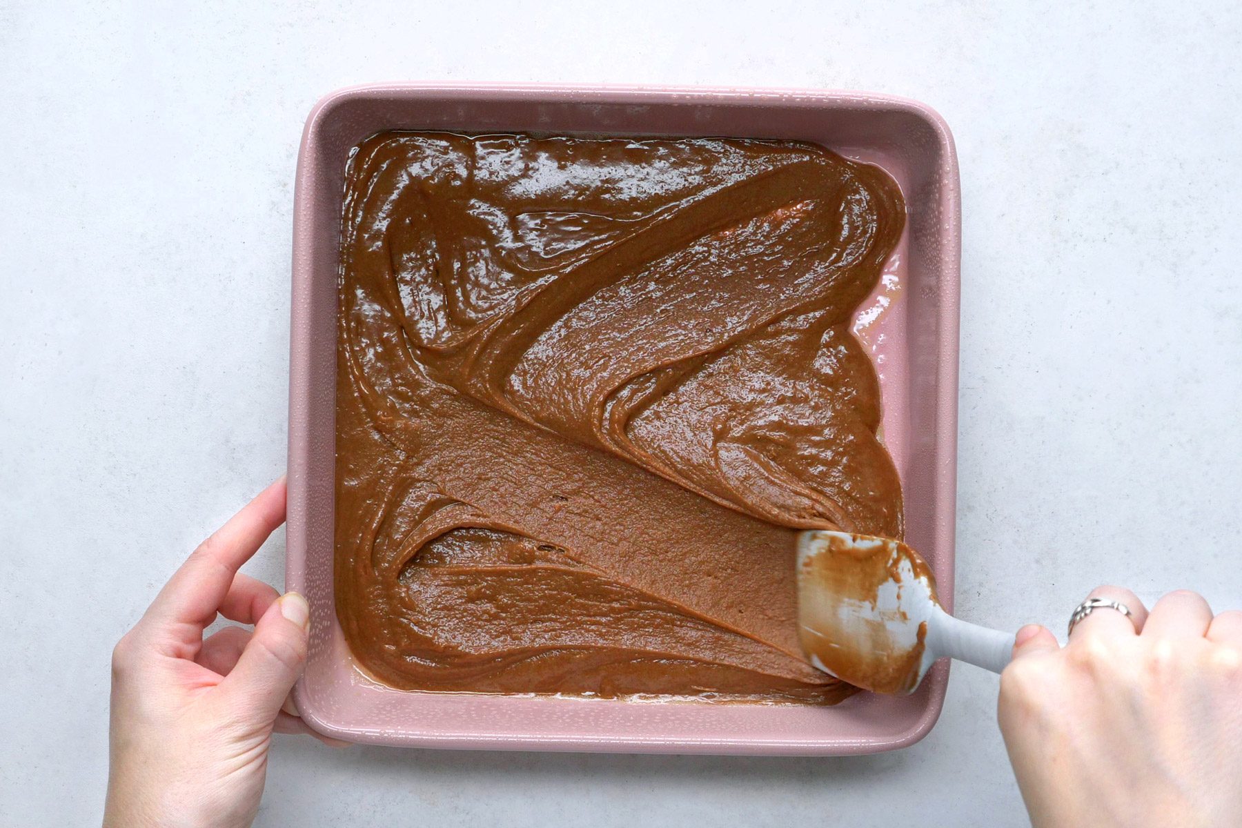 Fudge batter is being transferred to a square pan.