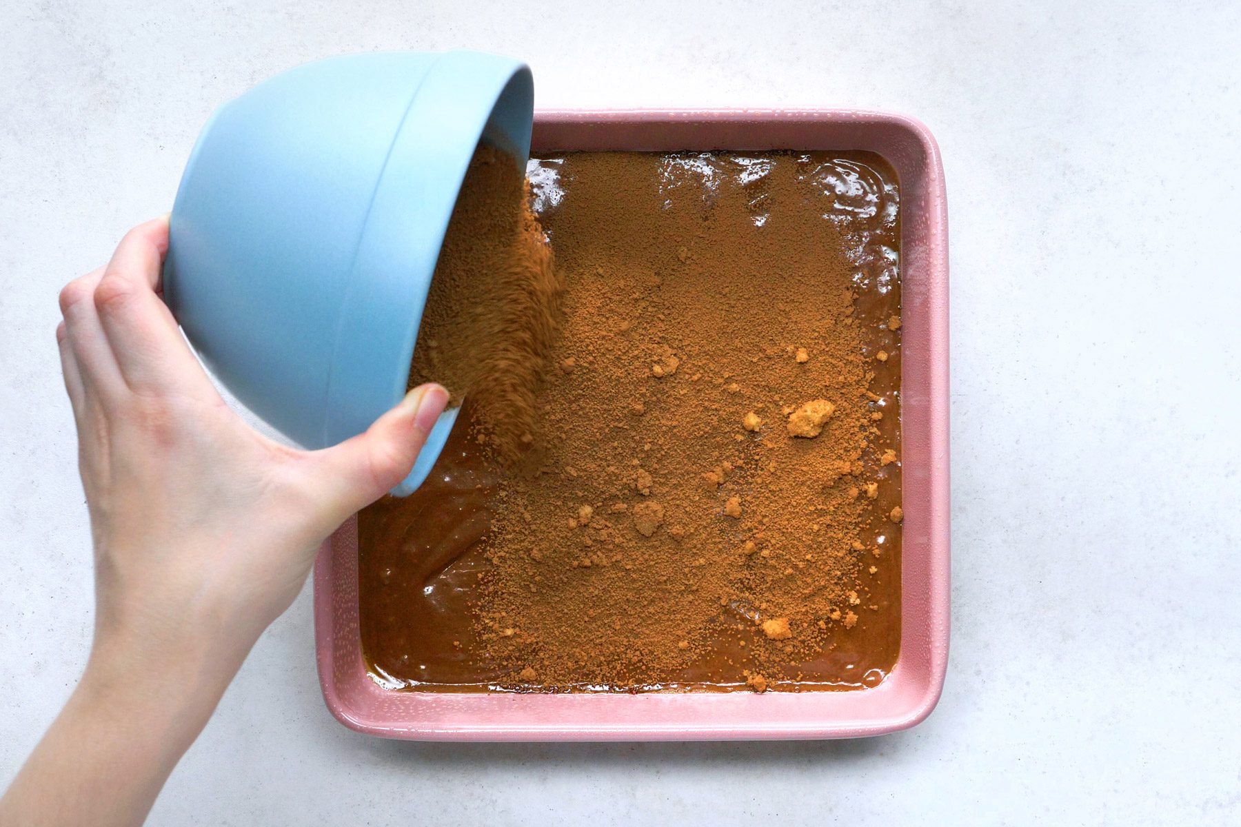 brown sugar and cocoa powder mix being sprinkled over fudge batter in a square pan.