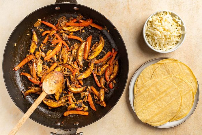 Taste of Home Mushroom Tacos recipe photo of the finished sauteed veggies with warm corn tortillas and cheese for topping.