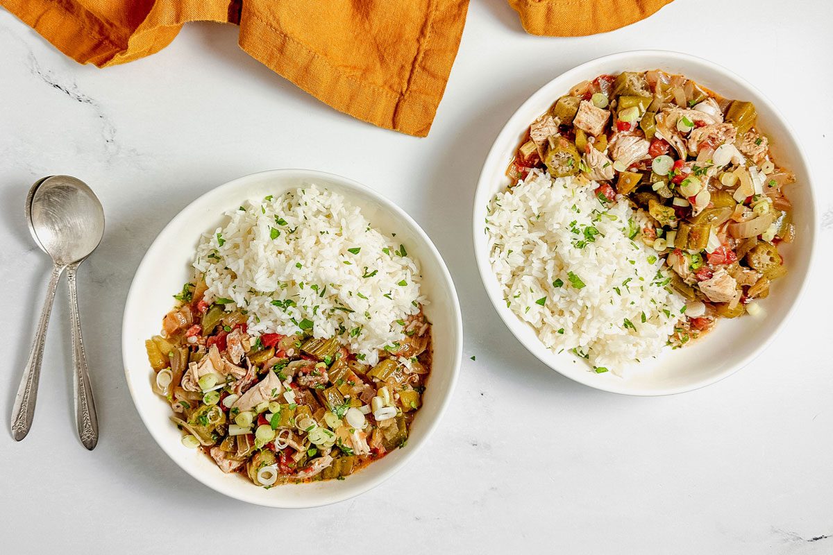 Taste of Home okra gumbo in white ceramic bowls with a linen napkin on a marble surface.
