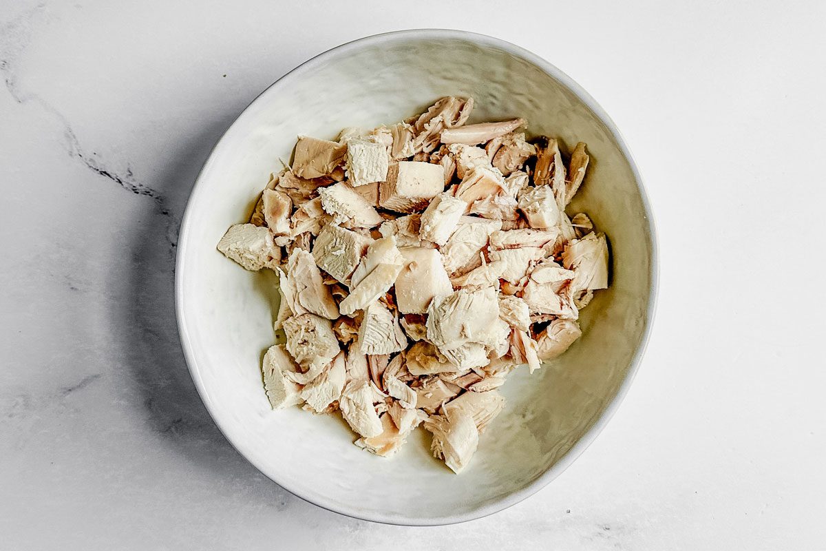 Cooked chicken for Taste of Home okra gumbo in a ceramic bowl on a marble surface.