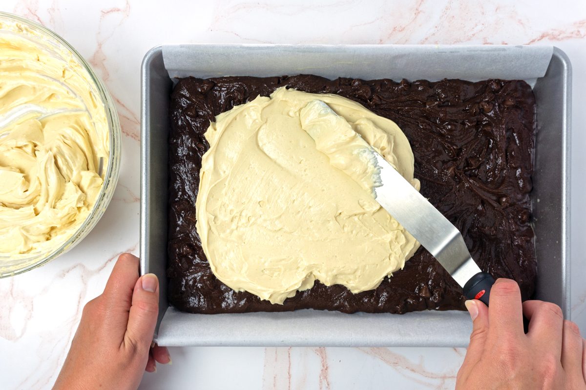 Brownie batter getting spread with a peanut butter cream cheese layer to make peanut butter swirl brownies for Taste of Home RMS 11889