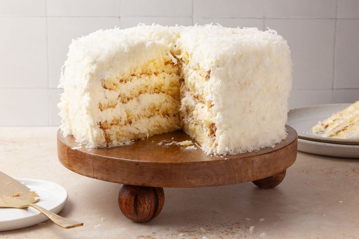 Taste of Home Pineapple Coconut Cake on a wooden platter, slices out, stack of plates