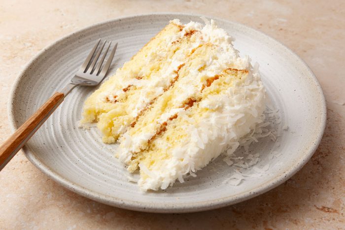 Single serving of Taste of Home Pineapple Coconut Cake on a plate with a fork with a wooden handle