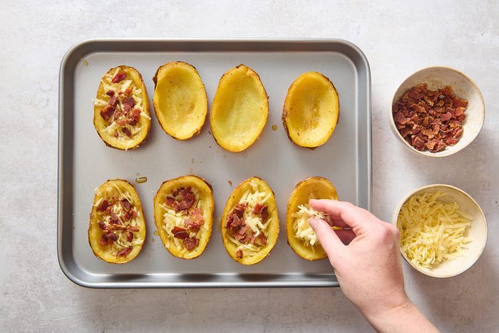 Sprinkling shredded cheese and bacon on the potato skins