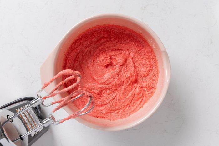 Eggs, vanilla extract, white vinegar and food coloring being added to the sugar and butter mix.