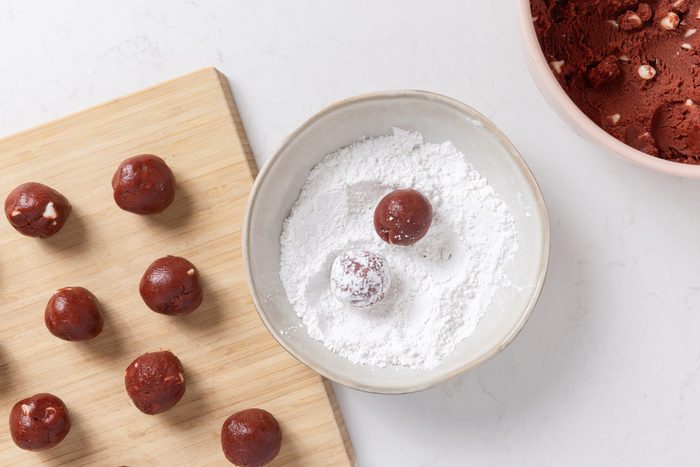 Cookie dough being shaped in balls and rolled in confectioner's sugar.
