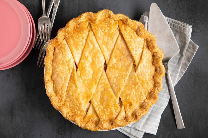 An overhead view of a freshly baked Rhubarb Custard Pie with plates, forks, and a pie server.