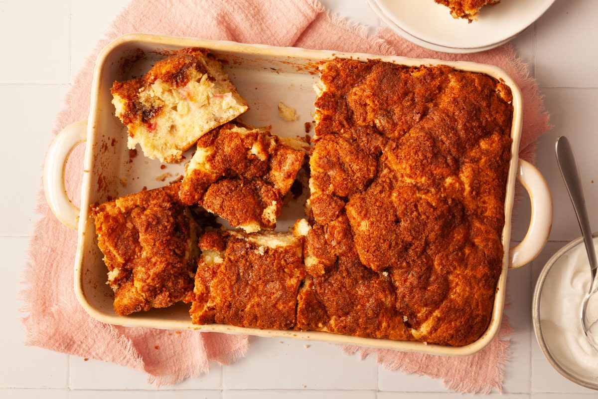Full yield of Taste of Home Rhubarb Coffee Cake in a 13x9 baking dish, on a pink linen, side of whipped cream in a bowl