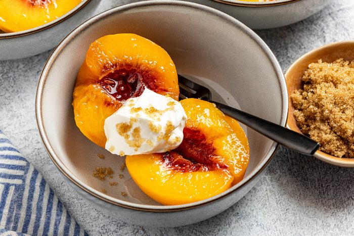 Taste of Home Spiced Peaches recipe photo of the poached peaches served into bowls with dollops of sour cream and sprinkle of bronw sugar.