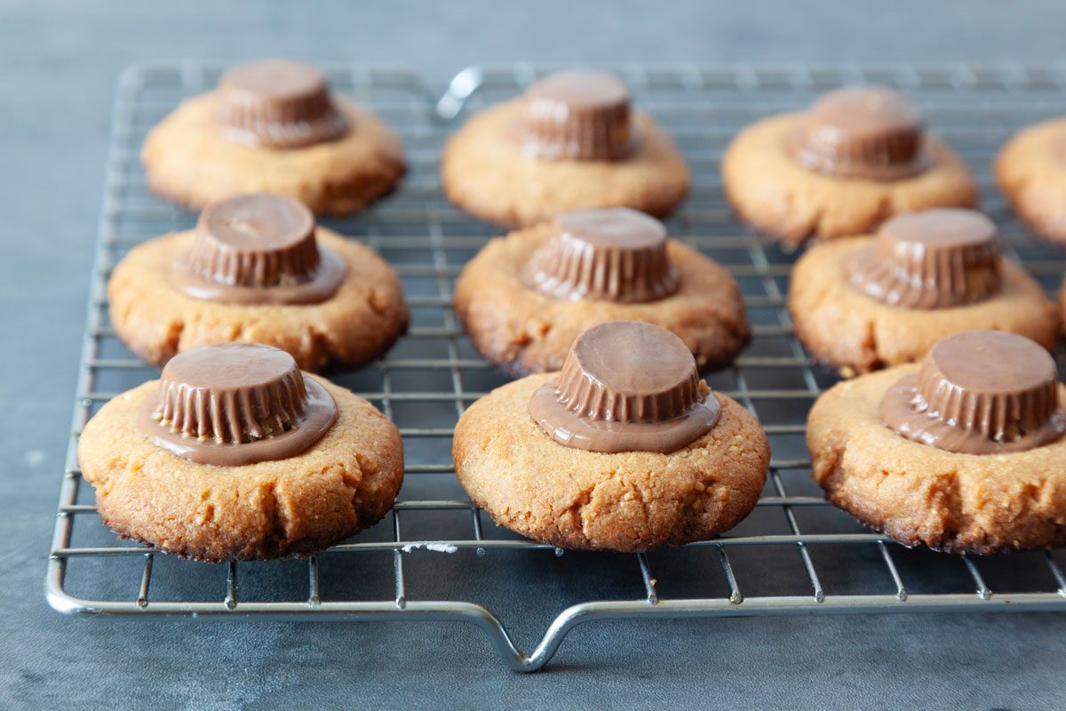 Step 3 of Taste of Home Spider Cookies is to bake the cookies and remove to wire wracks to cool before pressing a peanut butter cup into the cookie while still warm