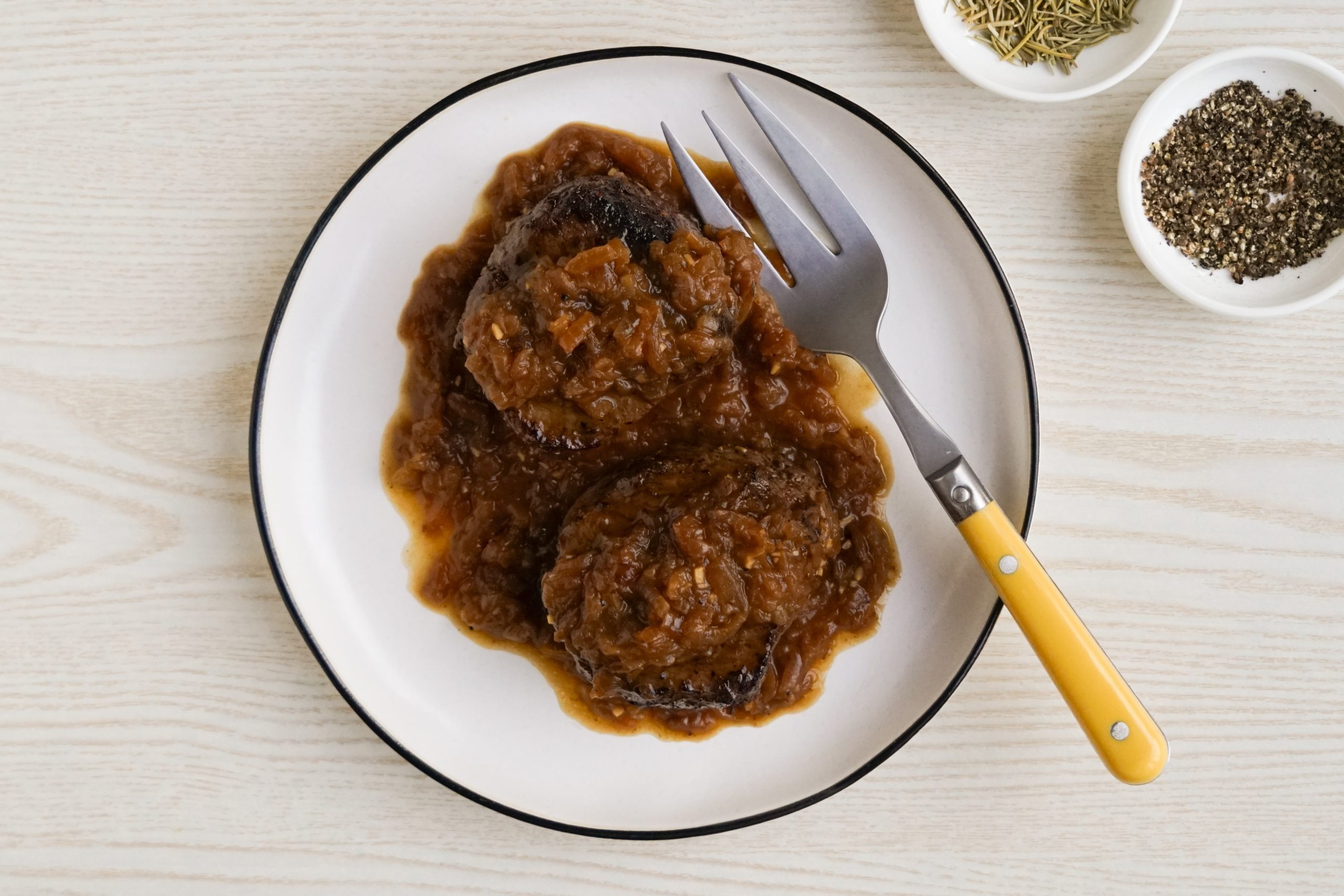 Filet mignon topped with caramelized onions on a platter with a yellow serving fork