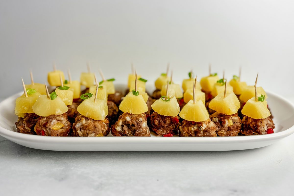 Taste of Home teriyaki meatballs topped with pineapple chunks in a white ceramic tray on a marble surface.