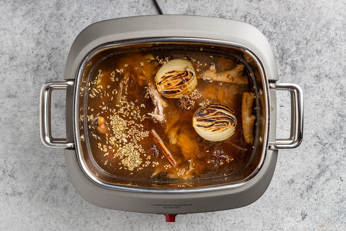 Taste of Home Thai Chicken Noodle Soup photo of the chicken bones, onion, ginger, spices and broth in a slow cooker.