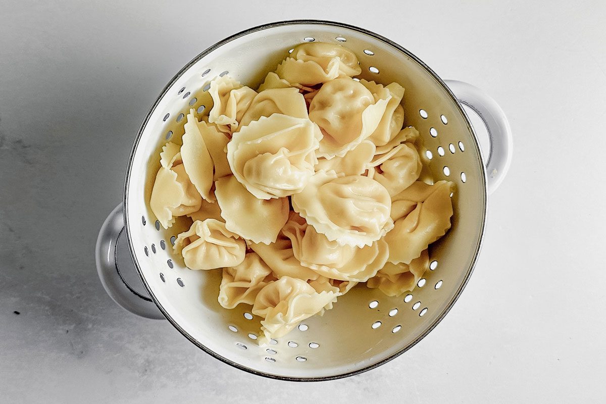 Cooked and drained tortellini in a white colander on a marble surface for Taste of Home tortellini carbonara.