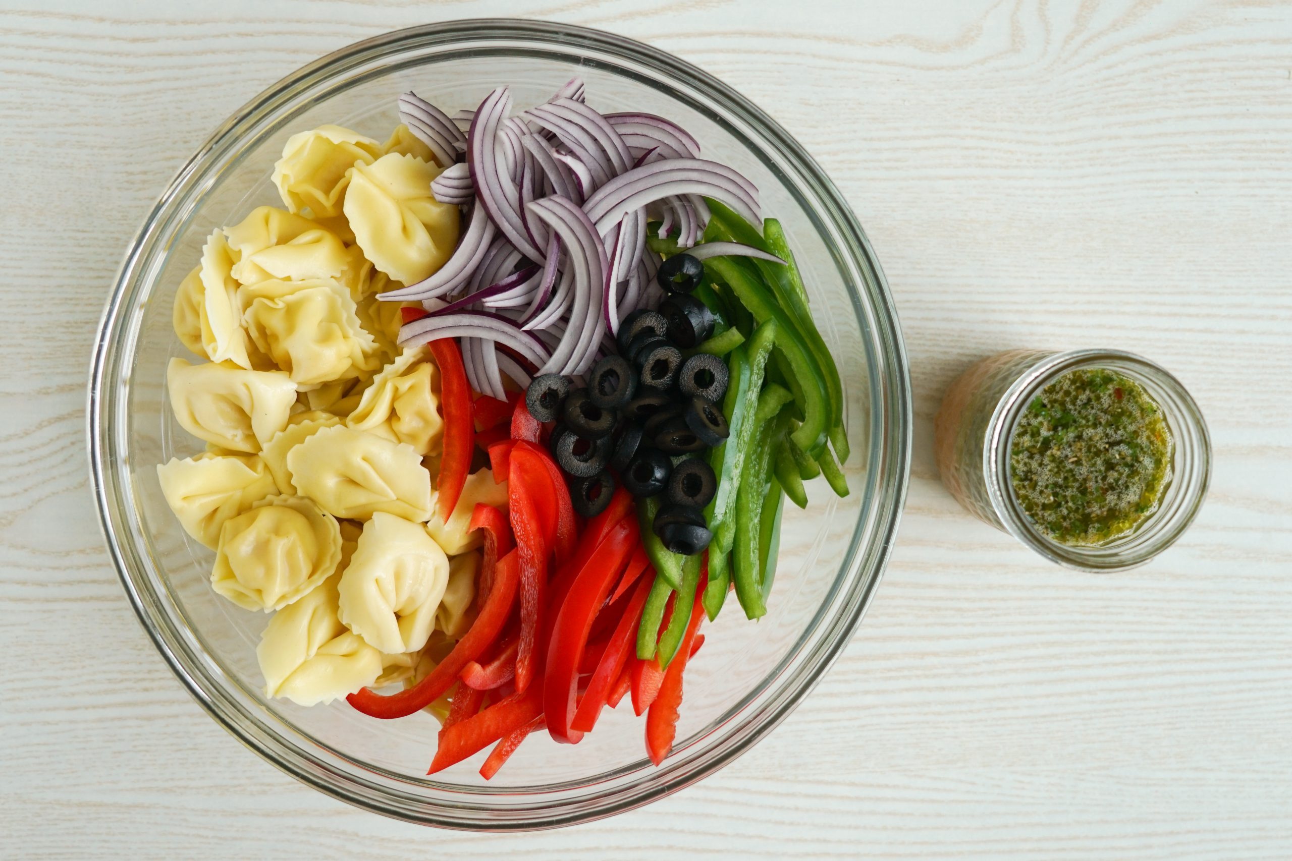 Tortellini pasta salad ingredients and dressing ready to be tossed