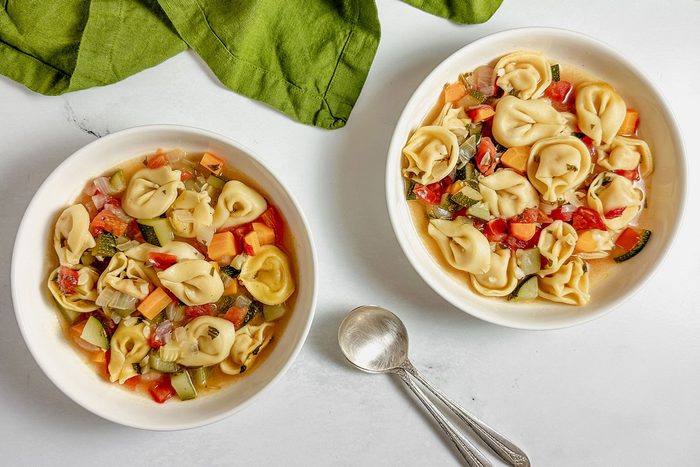 Taste of Home vegetarian tortellini soup in white ceramic bowls next to a green linen napkin.