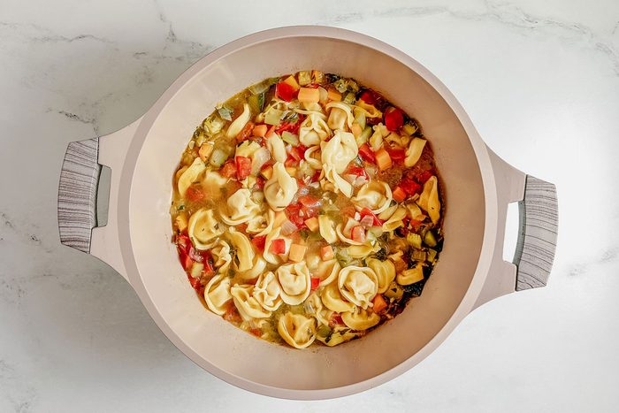 Taste of Home vegetarian tortellini soup in a Dutch oven on a marble surface.