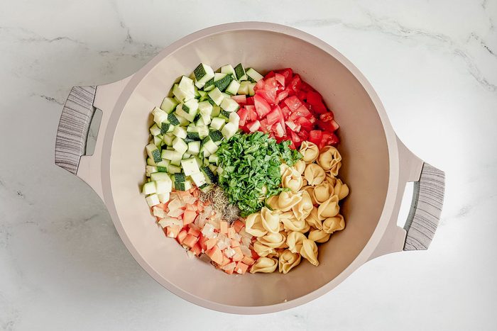 Ingredients for Taste of Home vegetarian tortellini soup in a Dutch oven on a marble surface.