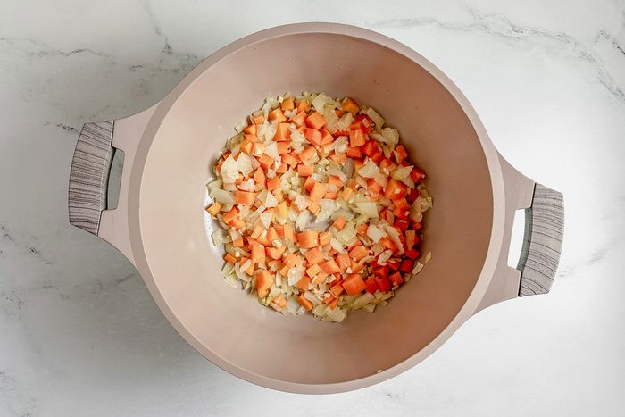 Carrots and onions in a Dutch oven on a marble surface for Taste of Home vegetarian tortellini soup.