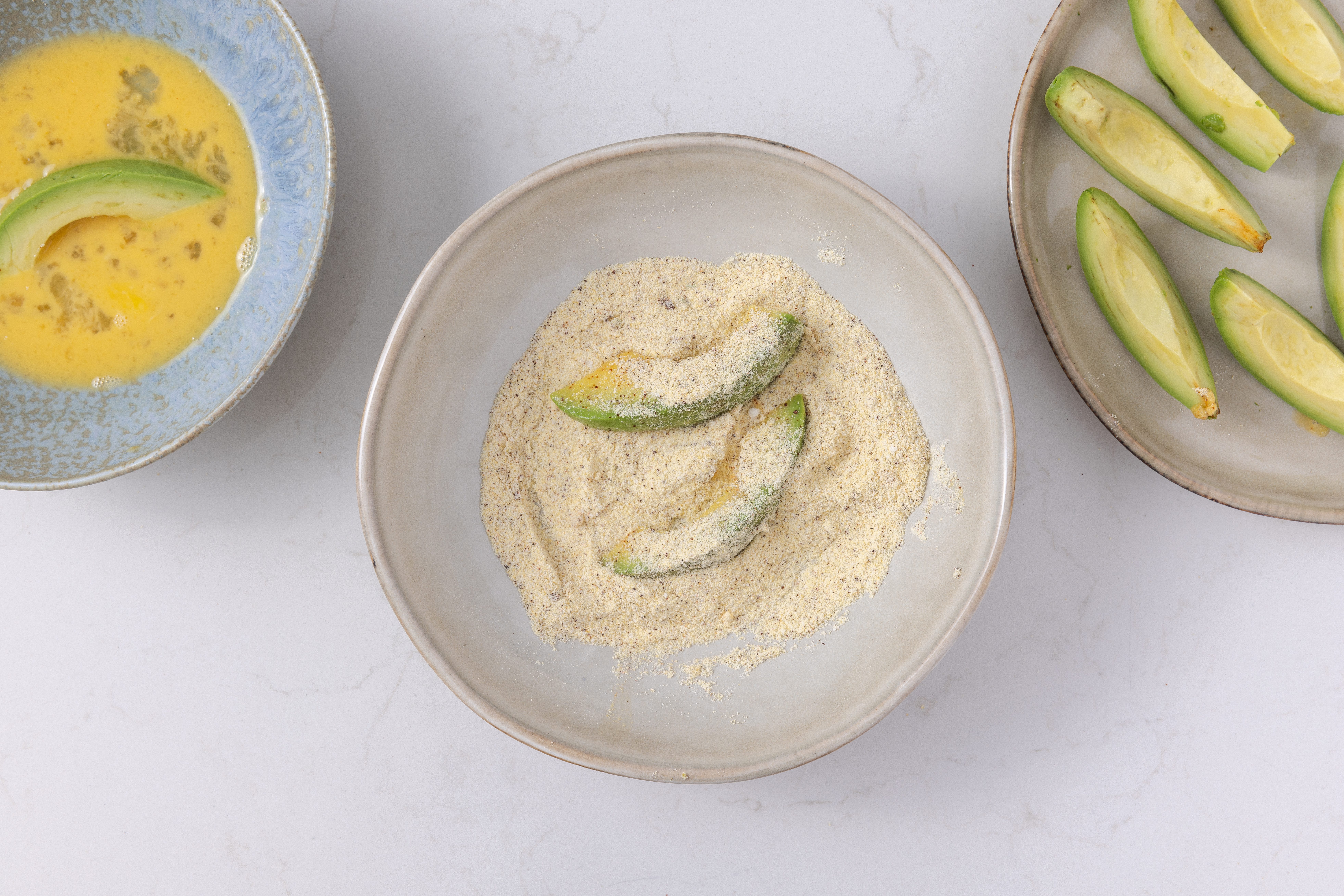 Avocado slices being dipped in the egg and cornmeal mixture.