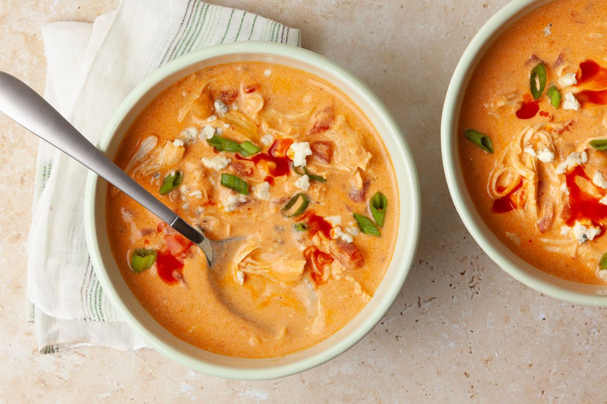 Two single servings of Taste of Home Buffalo Chicken Chili garnished with blue cheese, green onions and a drizzle of extra buffalo sauce