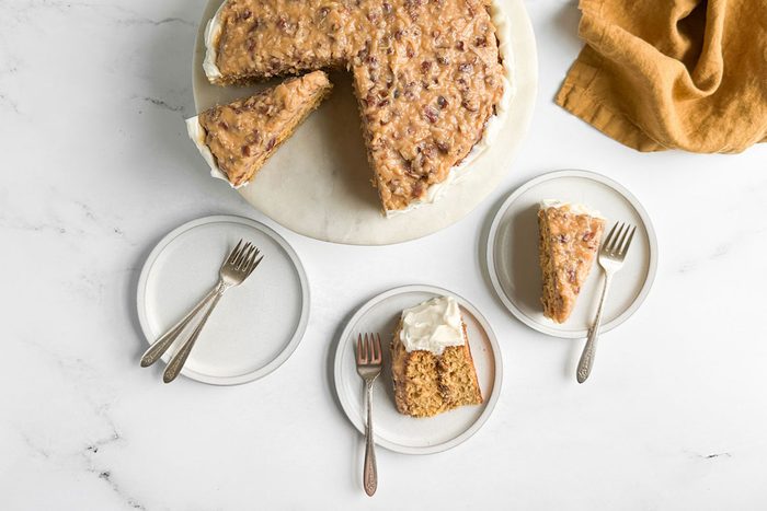 Taste of Home Butterscotch Cake on a marble and wood cake stand with slices of cake on white plates