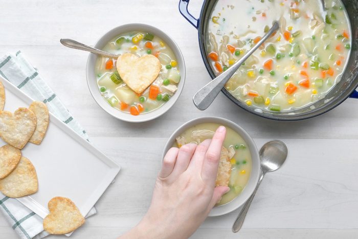 overhead shot; white wooden background; placing pie crust over the chicken potpie soup in a small bowl
