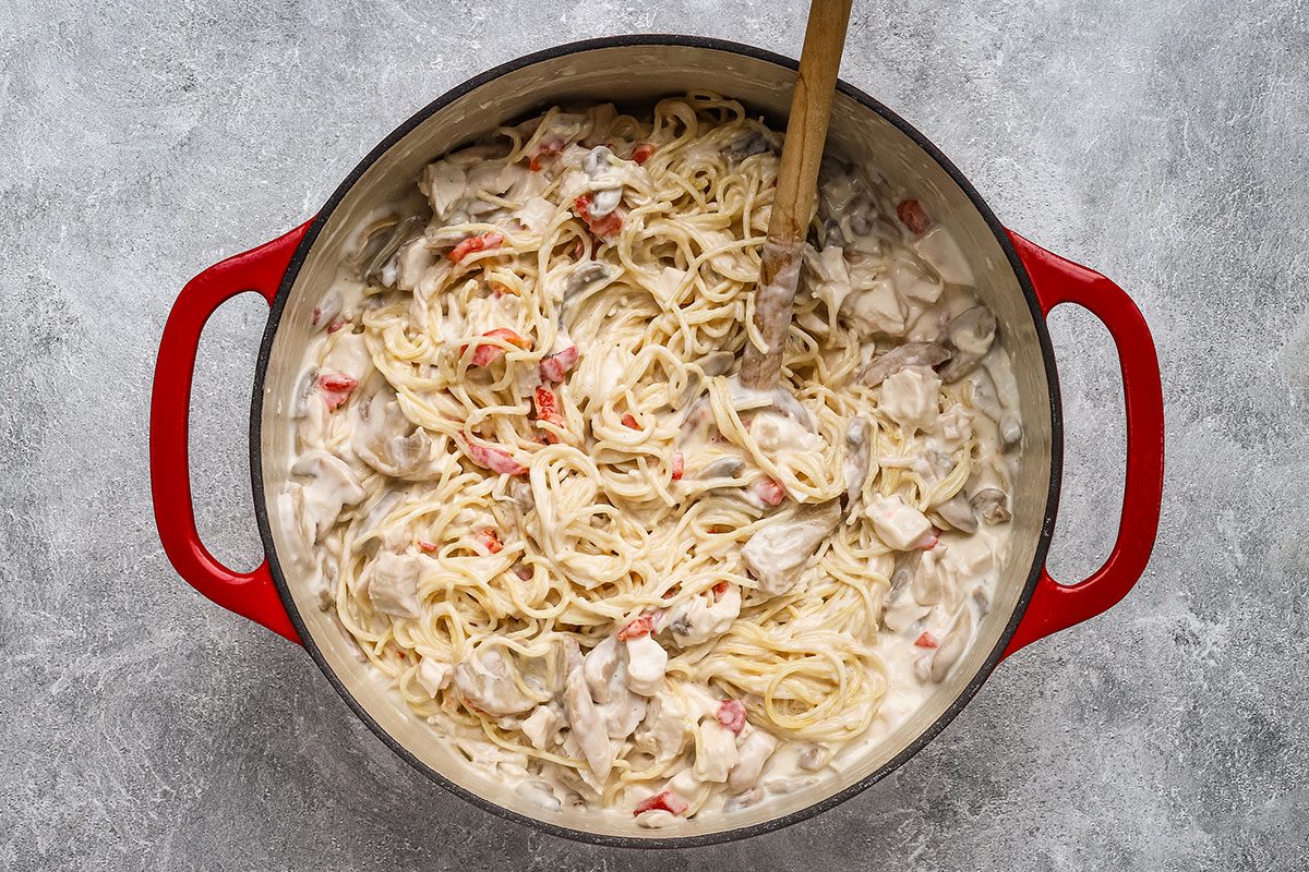 Combining the sauce with the pasta, chicken, and mushrooms, for a chicken tetrazzini recipe.