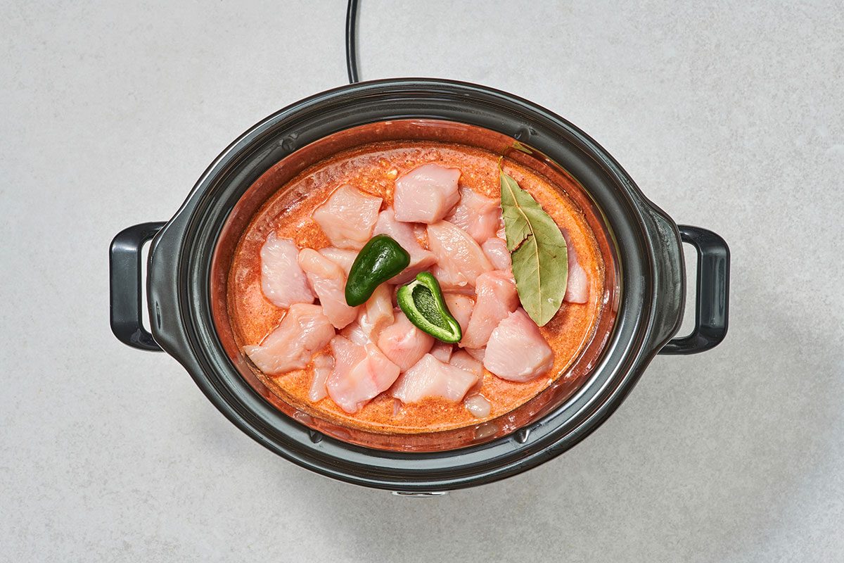 Cubed chicken jalapeño and bay leaf added to the sauce in a slow cooker 