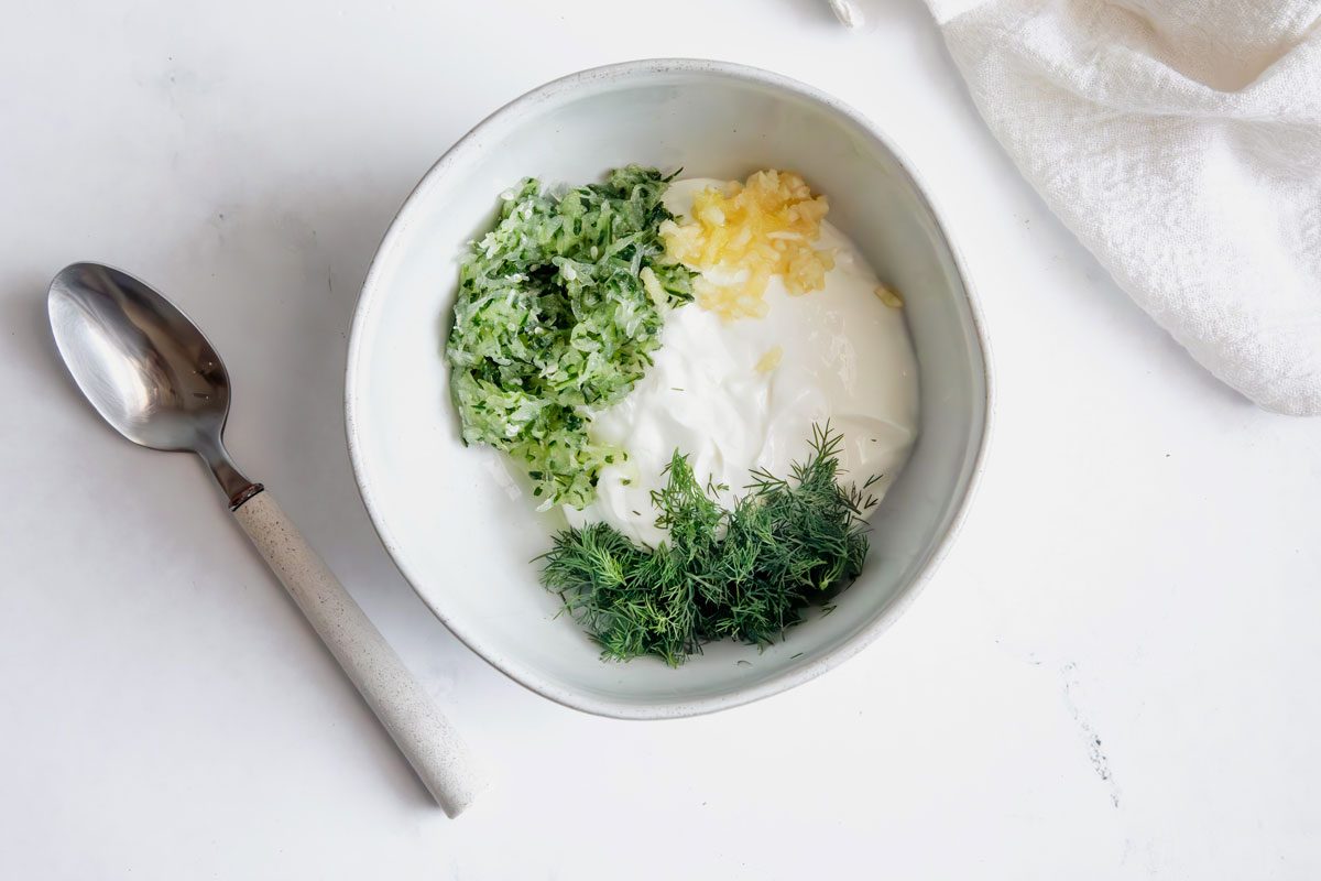 Overhead shot for Taste of Home Chicken Gyros with unmixed Tzatziki in a bowl on a marble surface.