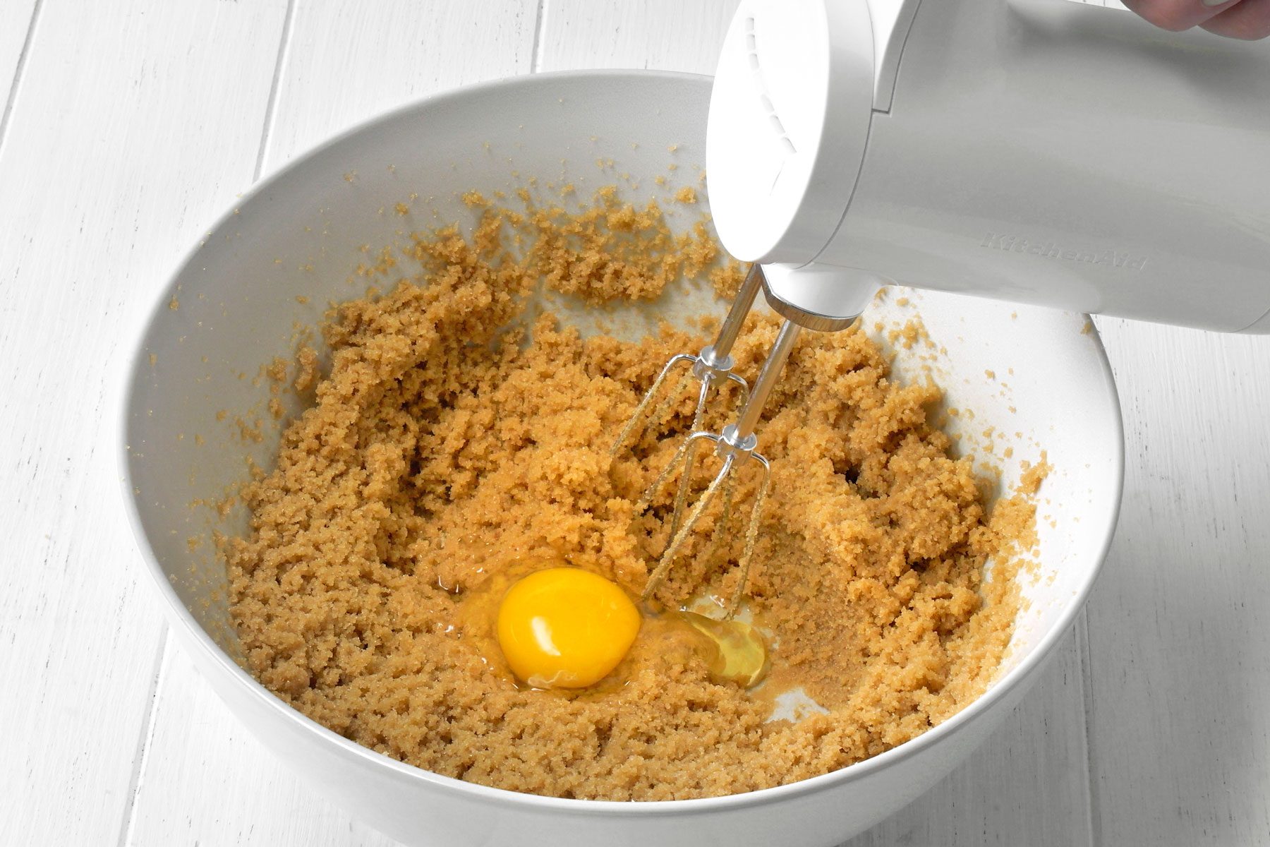Eggs being added to butter and brown sugar mixture in a large bowl.