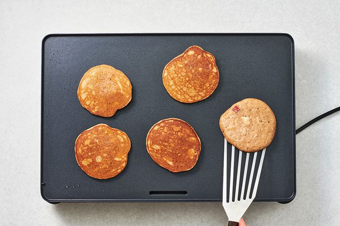 Cooked pancakes on the griddle with one being flipped
