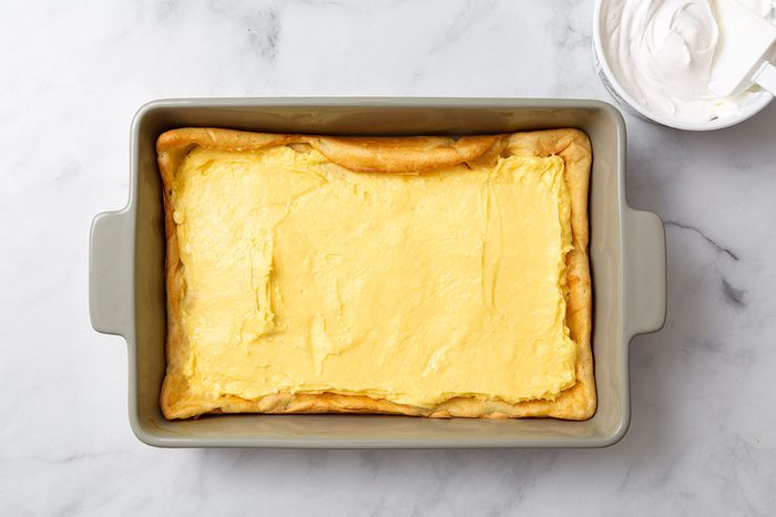 Pudding filling layered on top of pastry cake in a baking dish for step three of Cream Puff Cake recipe for Taste of Home
