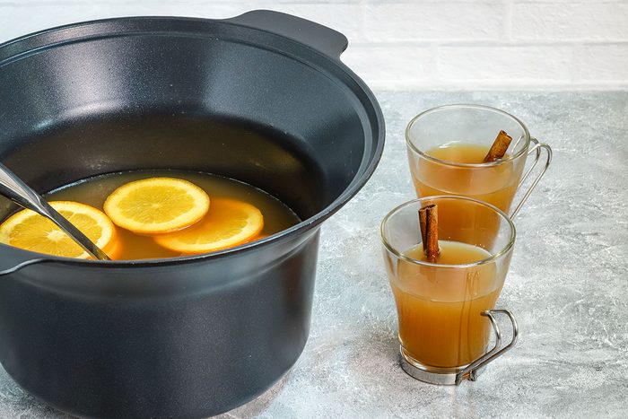 Spiced crockpot apple cider with ladle and filled cups on the side.