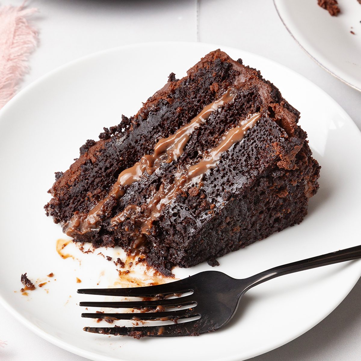 A few slices of Taste of home Brooklyn Blackout Cake on white and black plates, on white tiled surface, pink linen