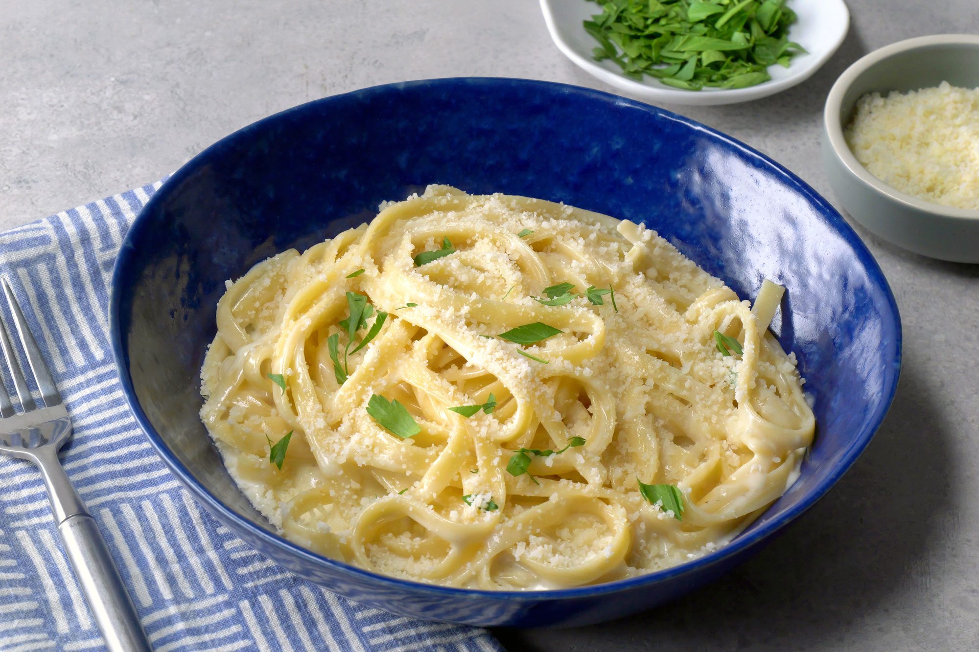 Fettuccine Alfredo pasta is topped with a sprinkle of freshly grated Parmesan cheese and a garnish of chopped parsley