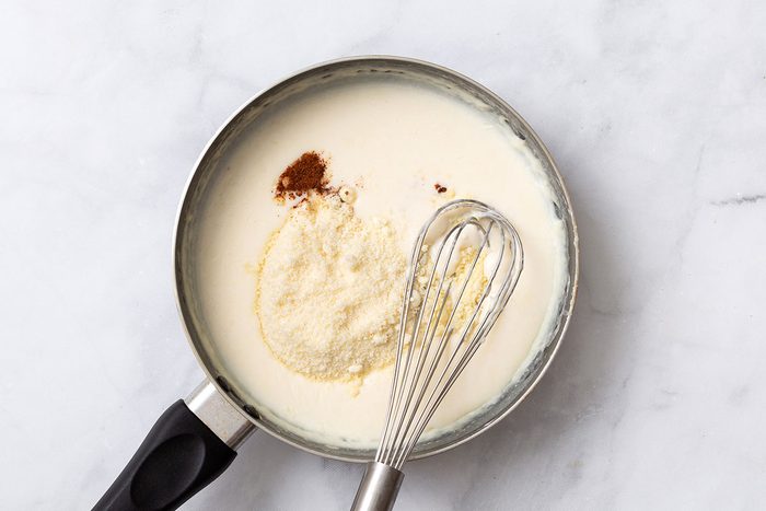Grated parmesan cheese and nutmeg being stirred into flour and milk mixture for sauce for Gnocchi Alfredo recipe for Taste of Home