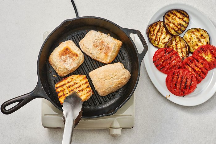 Ciabatta rolls grilling on a pan alongside slices of grilled eggplant and tomato