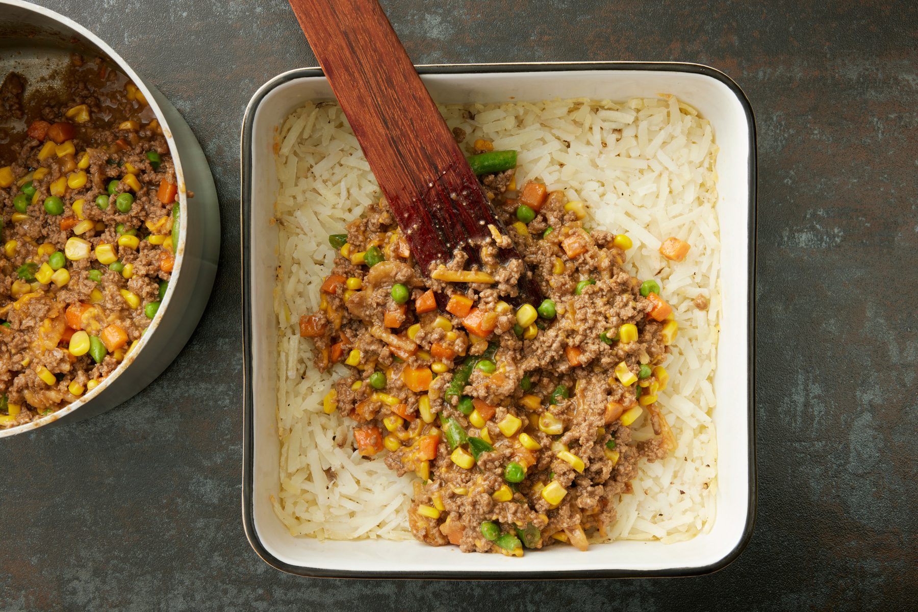 Overhead shot of pour over potatoes; bake 10 minutes; wooden flat spoon; dark texture surface