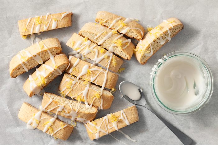 Overhead shot of Lemon Anise Biscotti; using glaze; whisk confectioners sugar and lemon juice in a small bowl; drizzle over biscotti; sprinkle with lemon zest; spoon; grey marble surface;