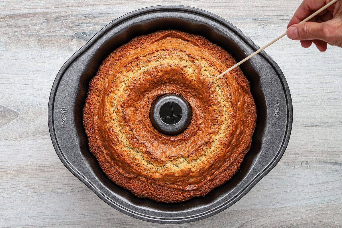 Testing the baked lemon poppy seed cake with a skewer.