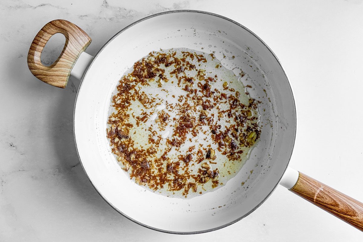 Anchovies and olive oil for Taste of Home Linguine with Clam Sauce in a white skillet on a marble surface