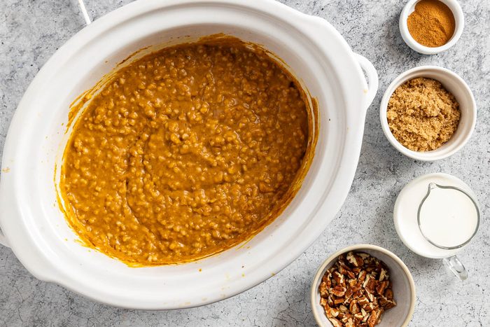 Taste of Home Pumpkin Oatmeal recipe photo of the cooked oatmeal in a slow cooker with sides of roasted pecans, milk, brown sugar and ground cinnamon to top.