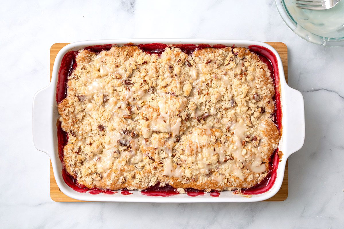 Baked Raspberry coffee cake in baking dish with drizzled vanilla glaze for step four of Raspberry Coffee Cake recipe for Taste of Home