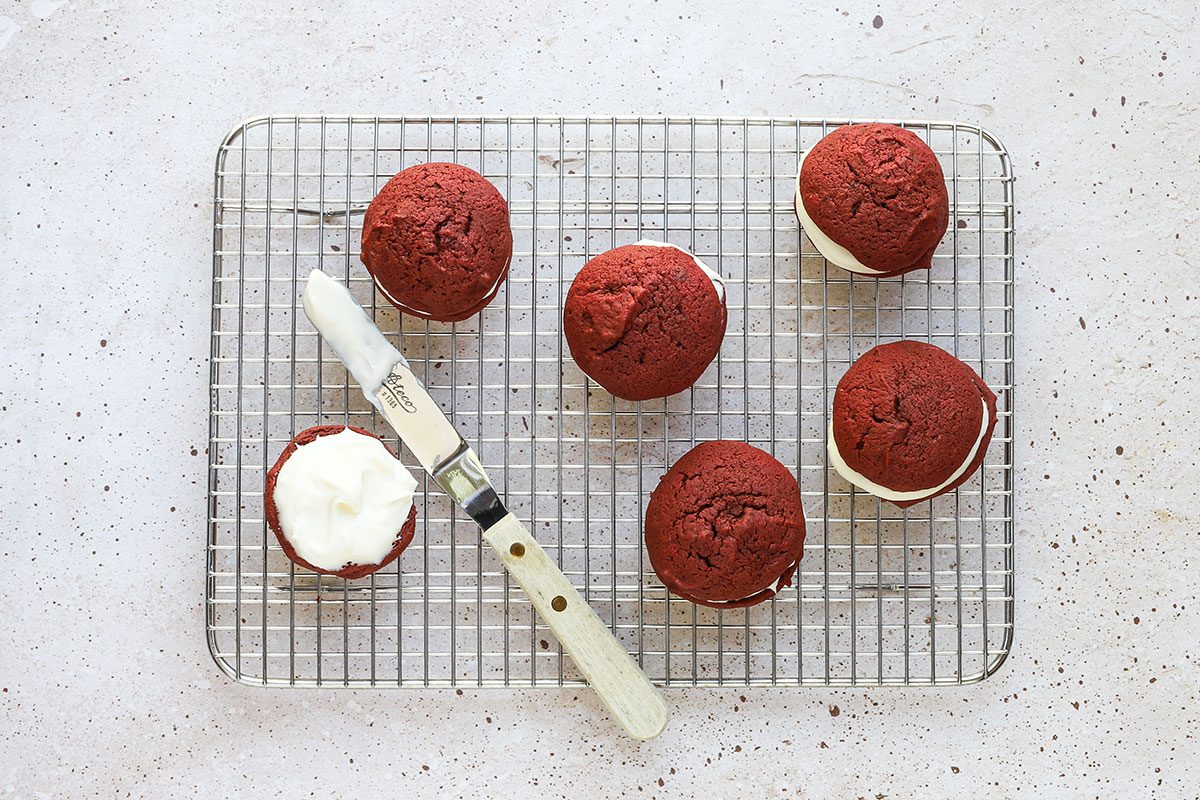 An icing spatula spreadding the cream cheese frosting or filling on red velvet whoopie pies.