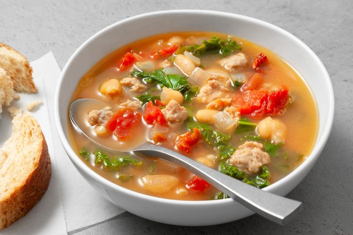 Table view shot of Italian Sausage Kale Soup; serve in a large bowl with bread; spoon; grey marble surface