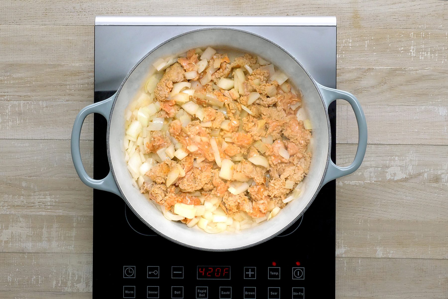 Overhead shot of a stockpot; cook sausage and onion over medium heat until no longer pink; breaking into crumbles; remove with a slotted spoon; induction; wooden background