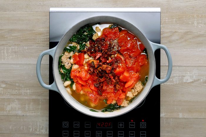 Overhead shot of the same pot; add garlic and pepper flakes cook 1 minute; add wine; cook 2 minutes longer; stir in sausage mixture and remaining ingredients; induction; wooden background